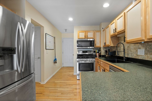 kitchen featuring dark countertops, decorative backsplash, appliances with stainless steel finishes, light wood-style floors, and a sink