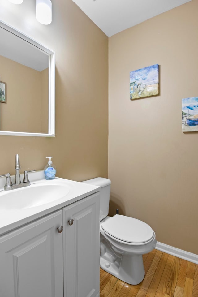 half bath featuring toilet, vanity, baseboards, and wood finished floors