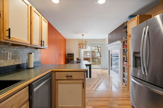 kitchen featuring tasteful backsplash, appliances with stainless steel finishes, a peninsula, light wood finished floors, and a chandelier