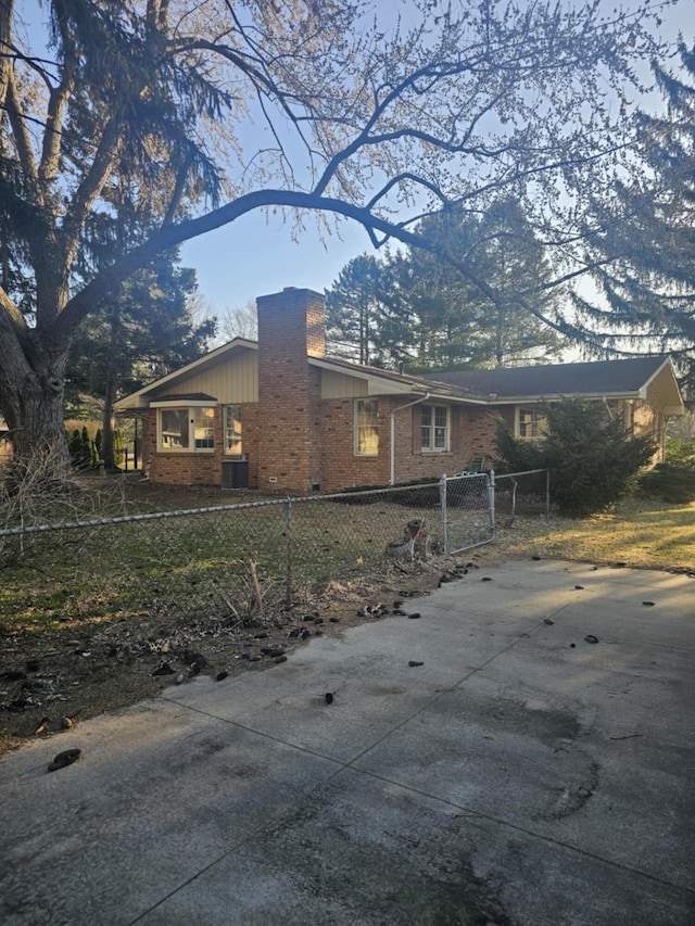 exterior space with brick siding, a fenced front yard, cooling unit, a chimney, and driveway