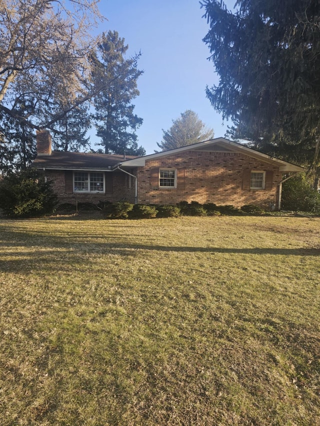 back of house featuring brick siding, a lawn, and a chimney