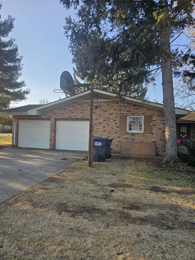 view of property exterior with an attached garage, brick siding, and driveway