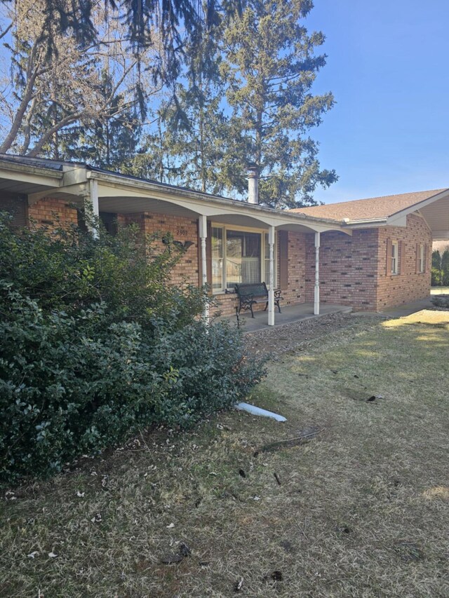 view of property exterior with brick siding, a lawn, and a patio area