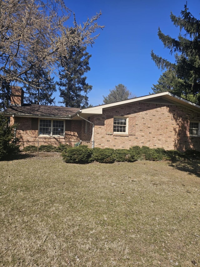 ranch-style house featuring brick siding, a chimney, and a front yard