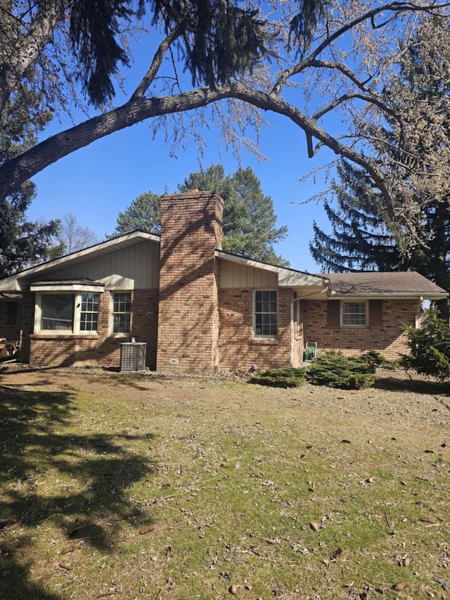 view of side of home with brick siding, board and batten siding, central AC unit, a chimney, and a yard