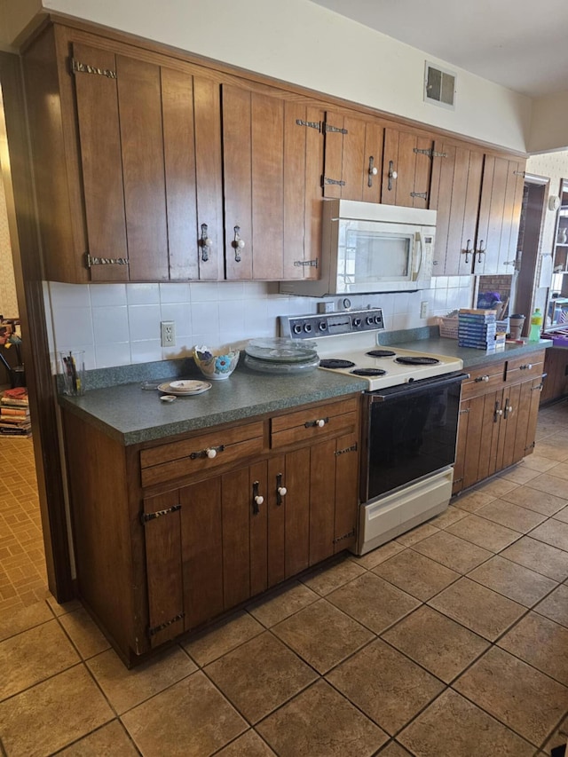 kitchen featuring visible vents, dark tile patterned floors, dark countertops, tasteful backsplash, and white appliances