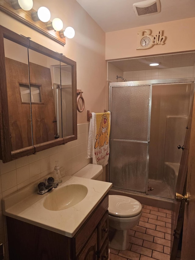 bathroom with visible vents, a shower stall, toilet, vanity, and tile walls