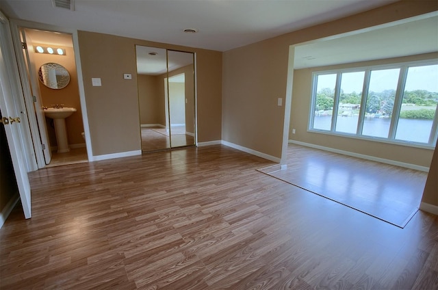 empty room with visible vents, wood finished floors, baseboards, and a sink