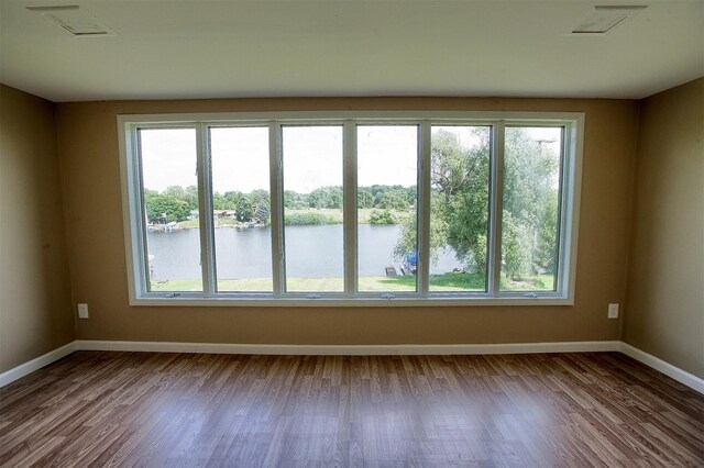 empty room with a wealth of natural light, wood finished floors, and a water view