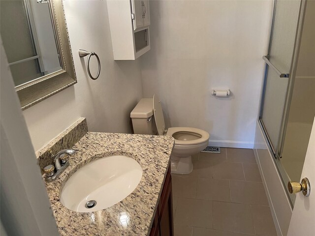 bathroom with toilet, baseboards, tile patterned flooring, enclosed tub / shower combo, and vanity