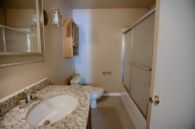 bathroom featuring vanity, baseboards, tile patterned floors, toilet, and combined bath / shower with glass door