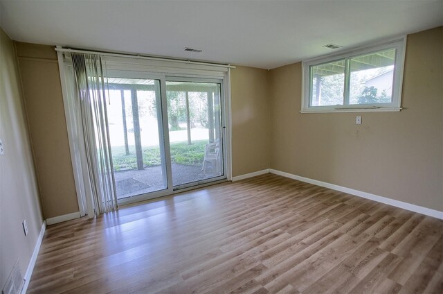 empty room featuring plenty of natural light, wood finished floors, visible vents, and baseboards