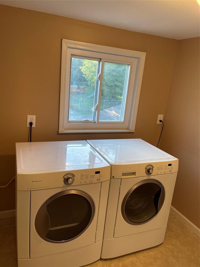 clothes washing area with light tile patterned floors, laundry area, washing machine and dryer, and baseboards