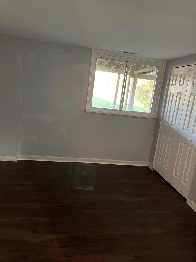 spare room featuring visible vents, baseboards, and dark wood-type flooring