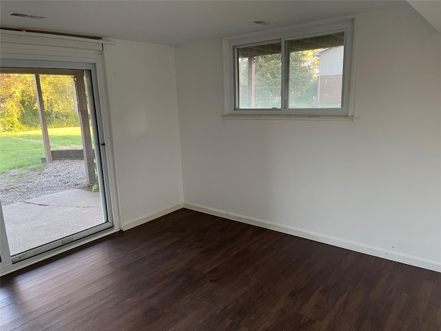 empty room featuring visible vents, dark wood-style flooring, and baseboards