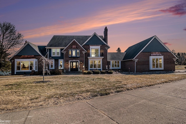 view of front of house with a front yard, a balcony, brick siding, and a chimney