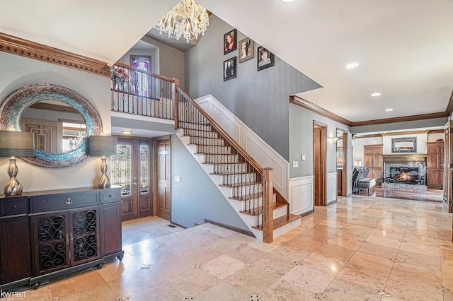 stairway featuring a wainscoted wall, recessed lighting, a lit fireplace, crown molding, and a chandelier