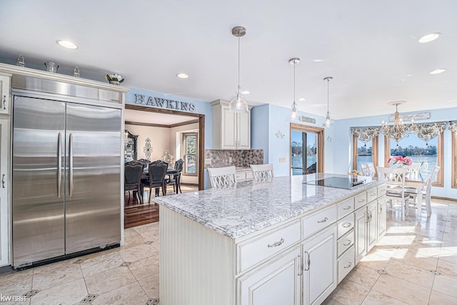 kitchen featuring tasteful backsplash, a kitchen island, black electric stovetop, stainless steel built in fridge, and light stone counters