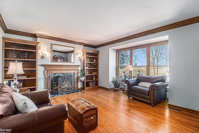 living area with light wood-type flooring, baseboards, a premium fireplace, and ornamental molding