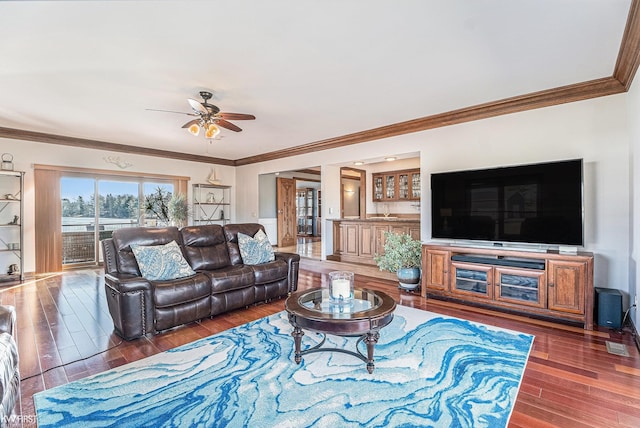 living room with a ceiling fan, crown molding, wood finished floors, and visible vents