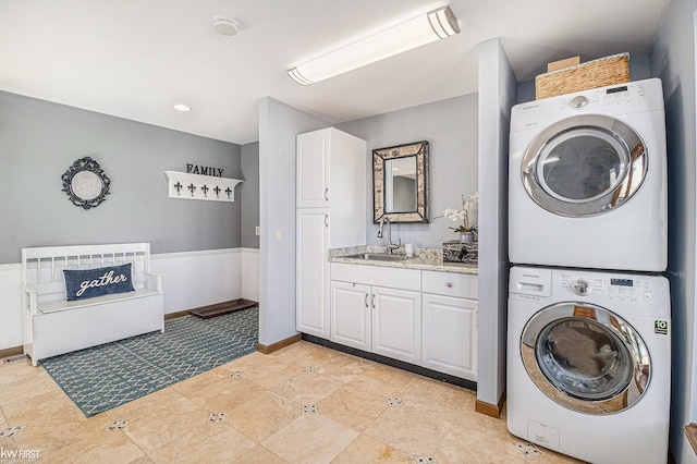 clothes washing area with a sink, baseboards, laundry area, and stacked washer / dryer