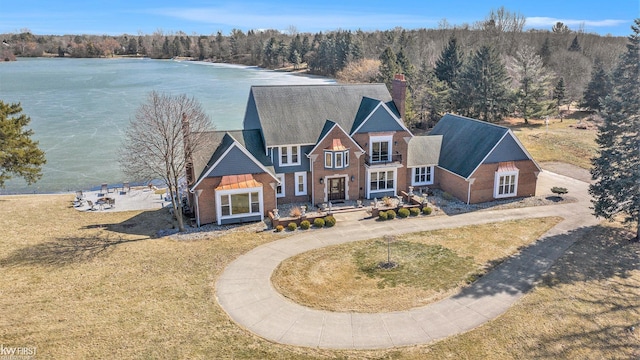 view of front of property featuring a front yard, a chimney, a water view, a view of trees, and brick siding