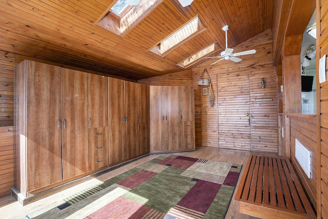 empty room featuring lofted ceiling with skylight, a ceiling fan, wood finished floors, wood walls, and wooden ceiling