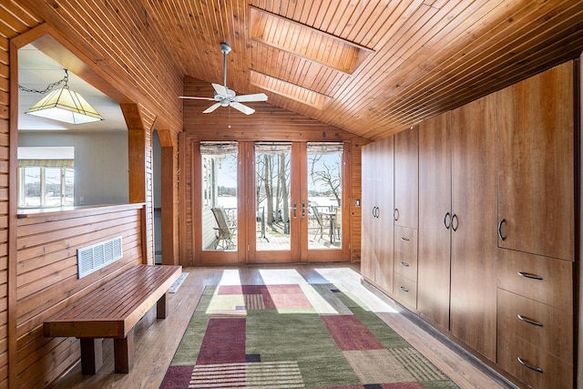 interior space with wood finished floors, lofted ceiling with skylight, a healthy amount of sunlight, and wood walls