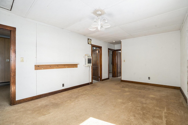 carpeted empty room featuring baseboards, heating unit, and a chandelier