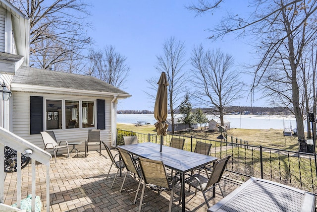 wooden terrace with a patio area, outdoor dining space, fence, and a water view