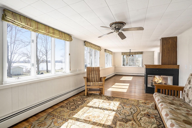 sunroom / solarium with a multi sided fireplace, baseboard heating, and ceiling fan