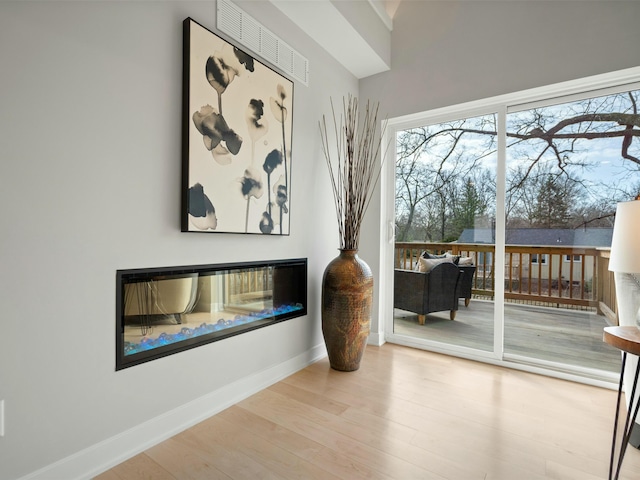 interior space with a glass covered fireplace, visible vents, baseboards, and wood finished floors