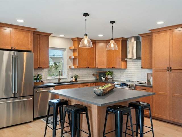 kitchen featuring a breakfast bar, a sink, stainless steel appliances, dark countertops, and wall chimney exhaust hood