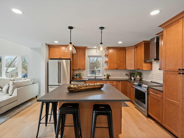 kitchen featuring dark countertops, light wood-type flooring, stainless steel appliances, wall chimney exhaust hood, and open shelves