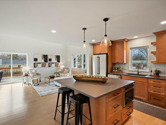 kitchen with a sink, backsplash, dark countertops, refrigerator, and light wood-style floors