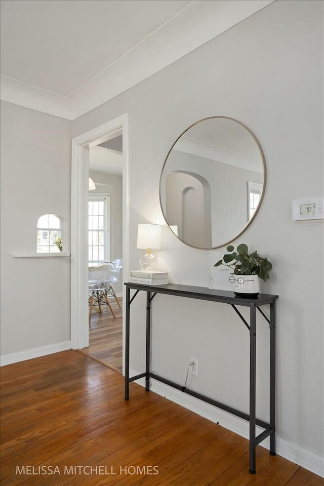 hallway with baseboards, wood finished floors, and crown molding