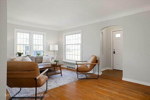 living room featuring light wood finished floors, visible vents, arched walkways, and baseboards