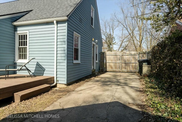 view of side of home with a gate, fence, roof with shingles, and a wooden deck