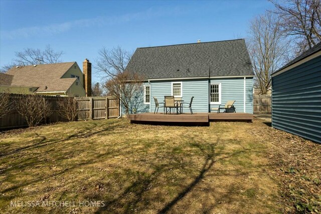 rear view of property featuring a deck, a lawn, a fenced backyard, and a shingled roof