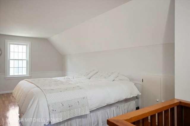 bedroom with baseboards, wood-type flooring, and vaulted ceiling