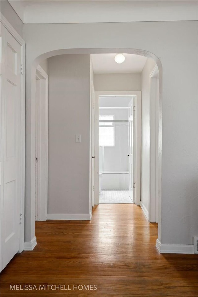 corridor featuring visible vents, wood finished floors, arched walkways, and baseboards