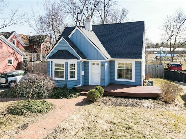 view of front facade featuring roof with shingles, a deck, a chimney, and fence