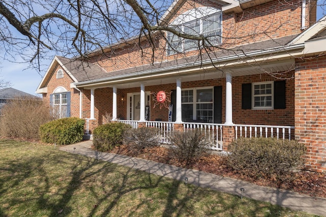 view of front facade with a porch, brick siding, and a front yard