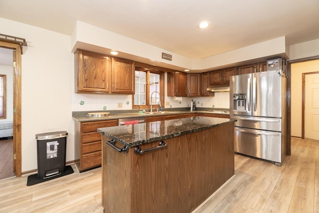 kitchen featuring a sink, a kitchen island, tasteful backsplash, stainless steel appliances, and light wood finished floors