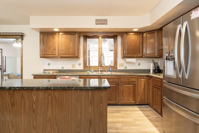 kitchen with dark stone countertops, light wood-style flooring, stainless steel refrigerator with ice dispenser, brown cabinetry, and a sink