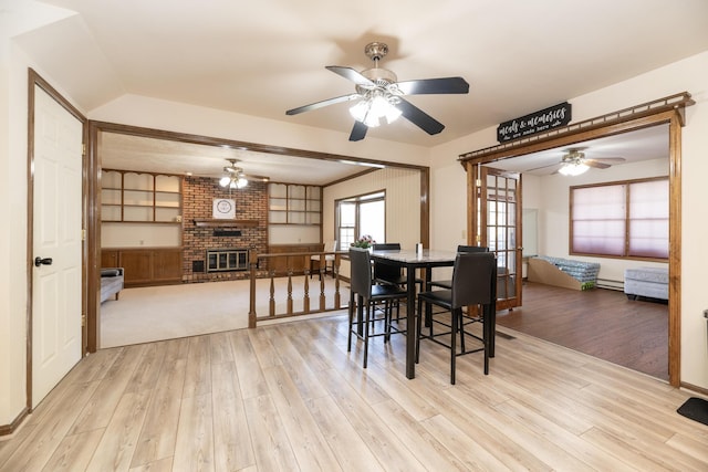 dining area featuring a baseboard radiator, a brick fireplace, light wood-type flooring, and ceiling fan