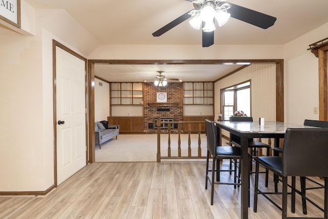 dining area featuring a ceiling fan, a fireplace, and light wood-type flooring