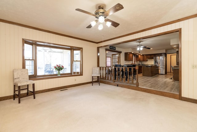 living room featuring visible vents, crown molding, ceiling fan, baseboards, and light carpet