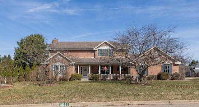 traditional-style house featuring a porch, brick siding, a front yard, and a chimney