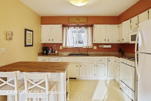 kitchen with butcher block countertops, a sink, white appliances, light tile patterned flooring, and white cabinets